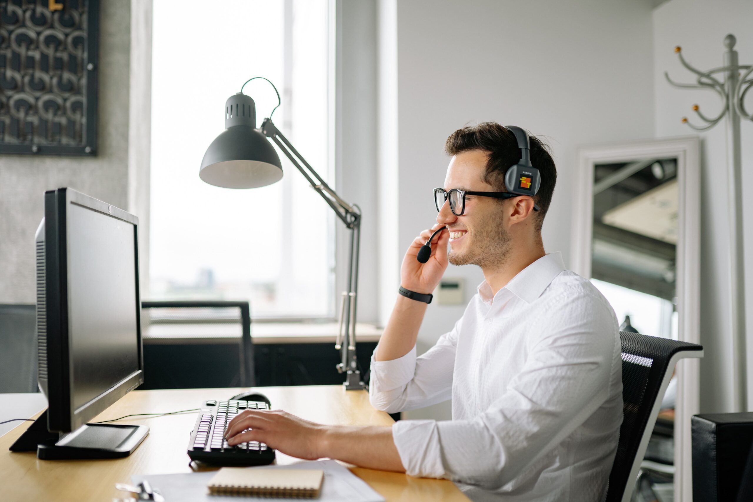 a man with a headset sitting at a desktop computer.