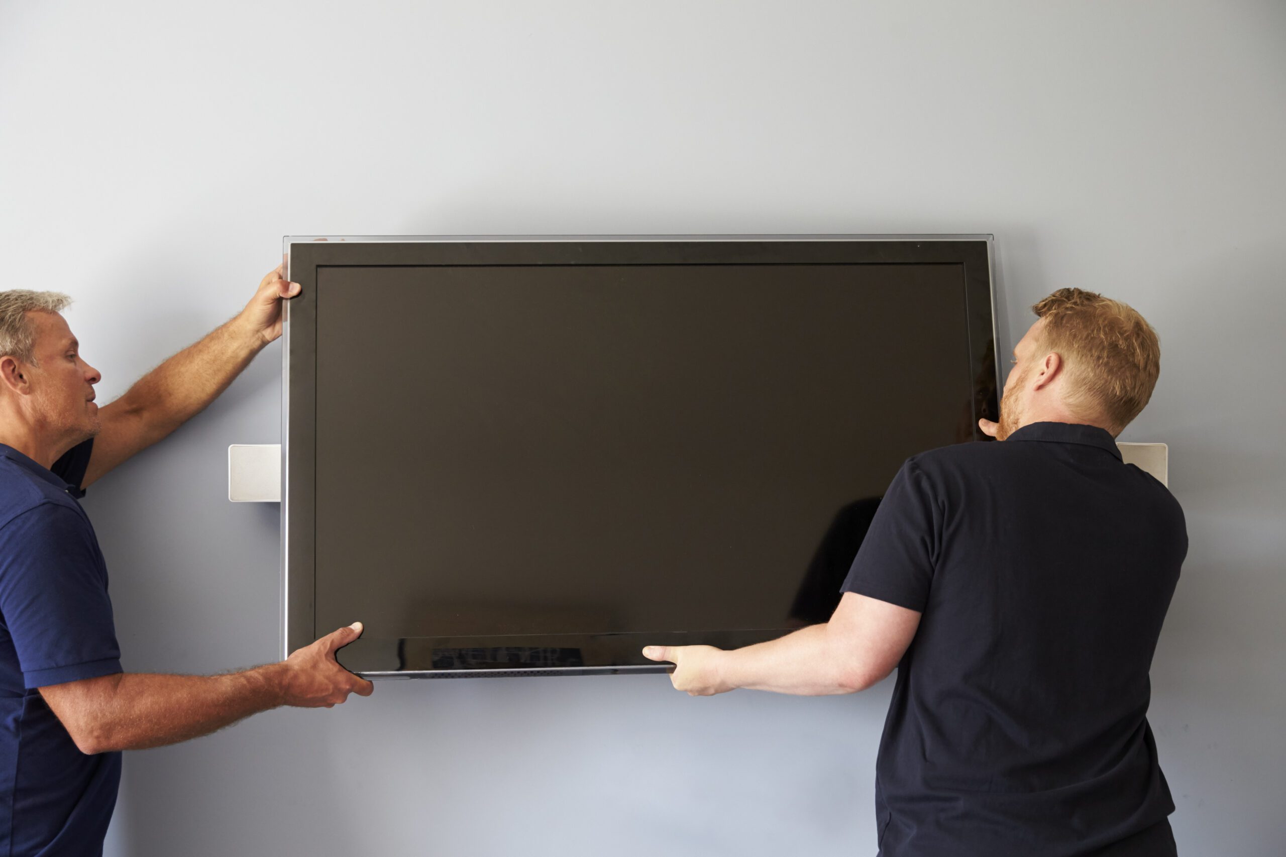 two men lifting a tv based on how high it should be mounted